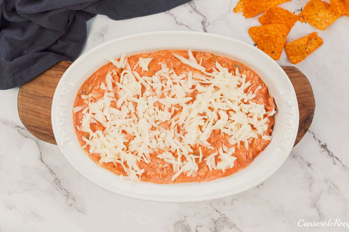 final step of making hot sausage dip by topping with cheese prior to baking