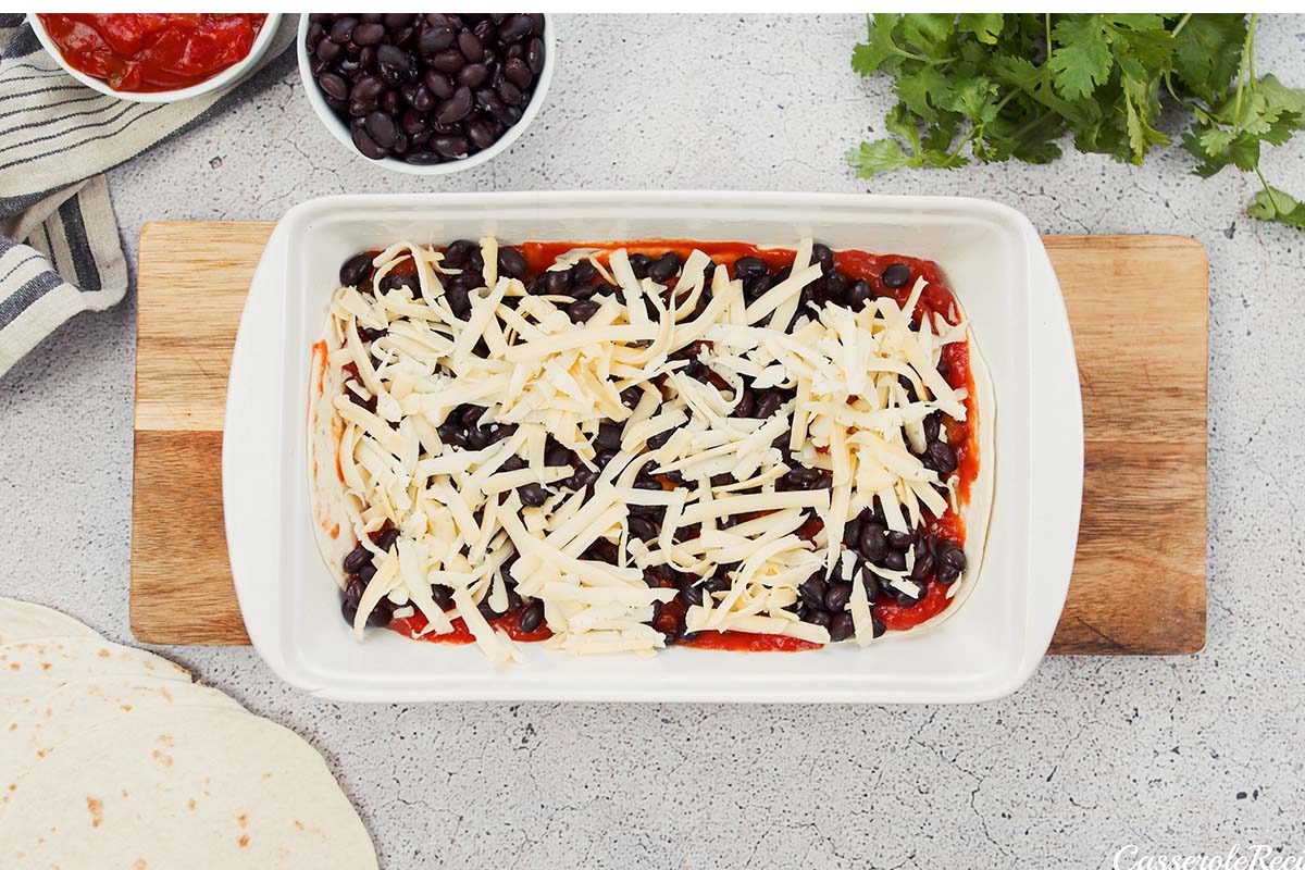 adding cheese layer to make huevos rancheros casserole in a casserole dish