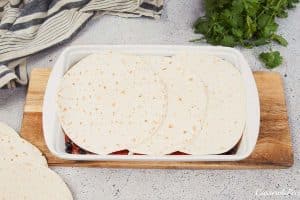 layering ingredients into a baking dish to make huevos rancheros casserole