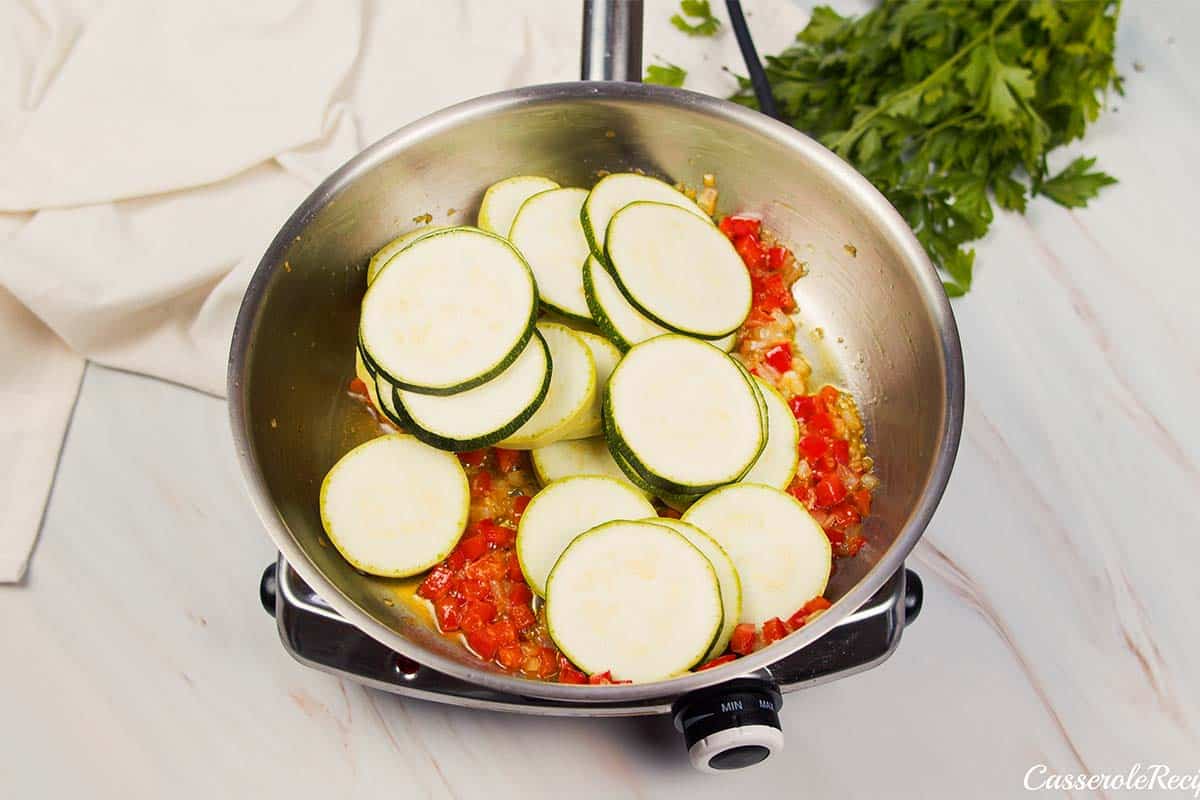 sliced squash being cooked down in a pan with other ingredients to make mini squash casserole