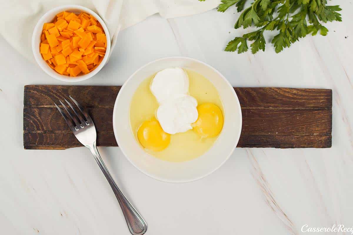 eggs and other ingredients being mixed together in a bowl to make mini squash casserole