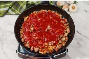 tomato sauce being added to meat mixture and other ingredients to make noodle pizza casserole