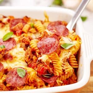 spoon lifting a serving of noodle pizza casserole from a baking dish