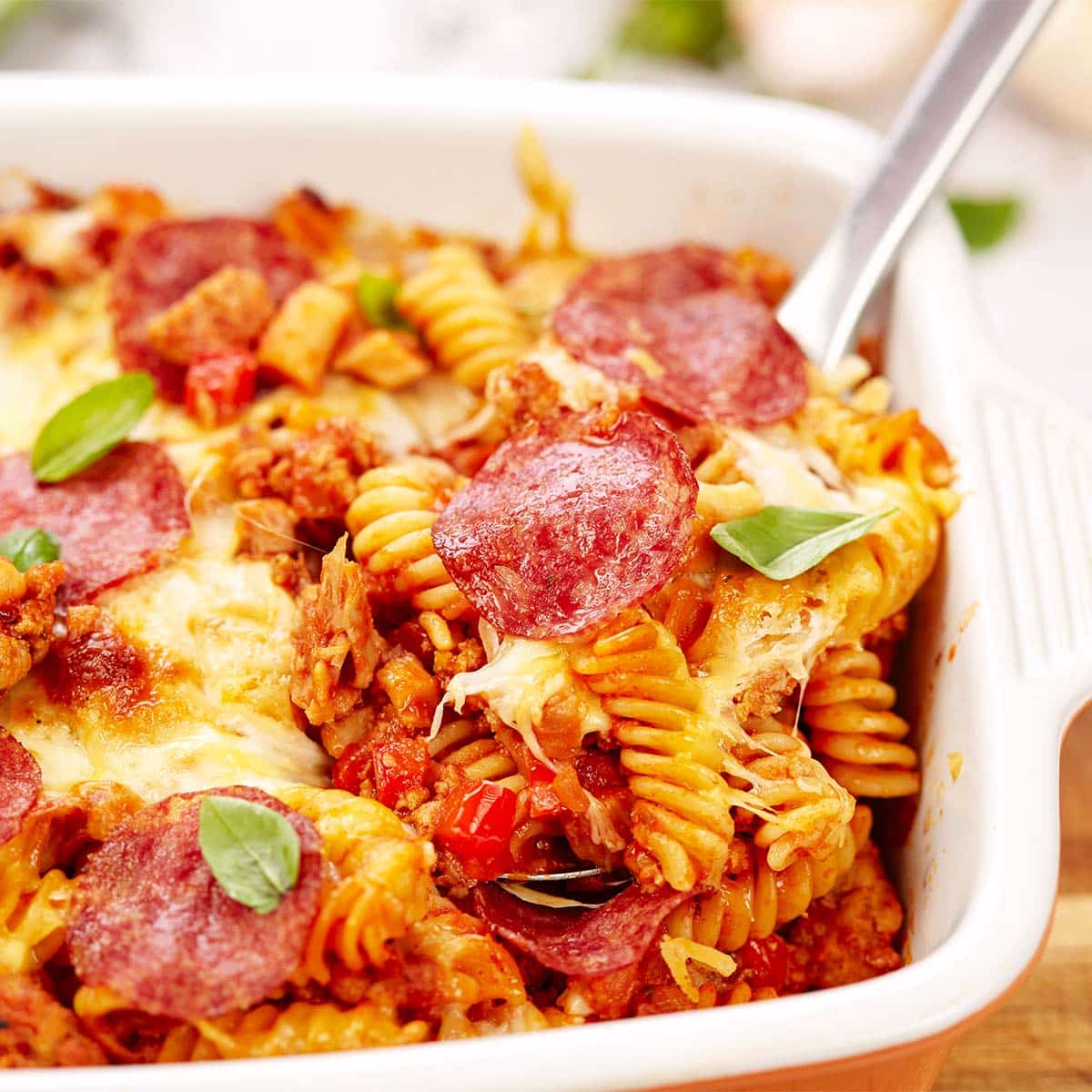spoon lifting a serving of noodle pizza casserole from a baking dish