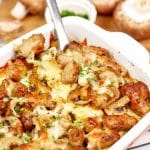 spatula lifting a serving of polenta with sausage and mushrooms from a casserole dish