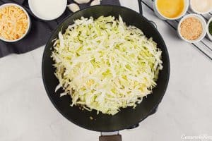 cabbage being added to a pan to sautee it to make polish cabbage, potato and bacon casserole