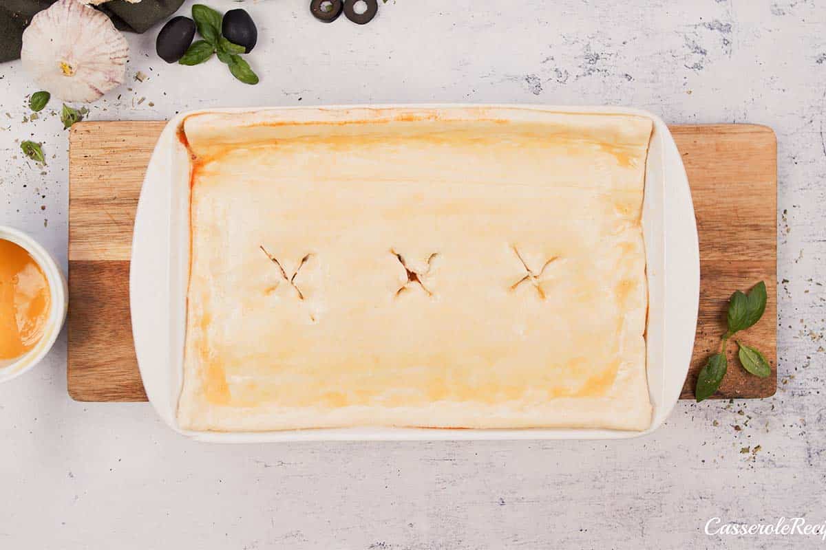 final step of topping upside down pizza casserole with a sheet of puff pastry before baking