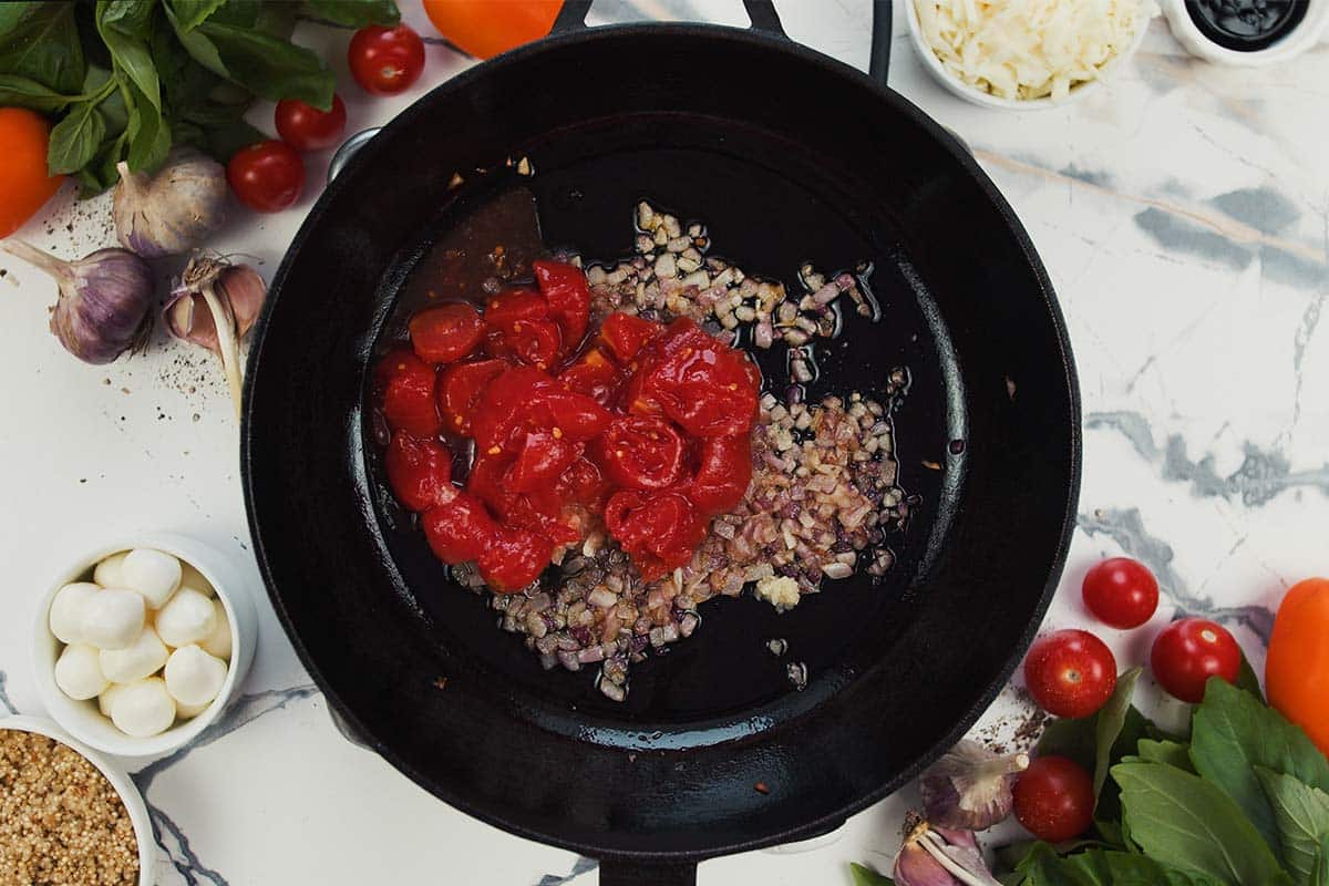 combining tomato paste and other ingredients in a saute pan to make Caprese Quinoa Bake