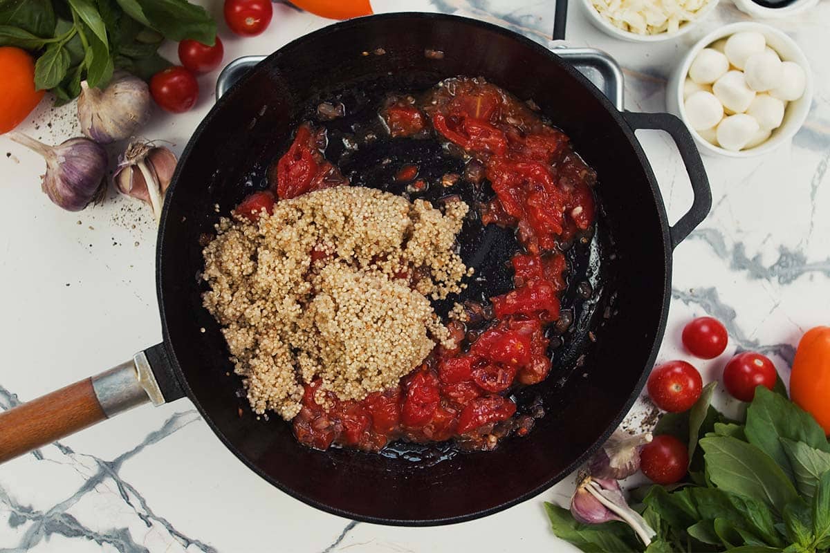 adding quinoa to tomato paste and other ingredients in a saute pan to make Caprese Quinoa Bake