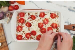 topping the filling of a casserole dish of Caprese Quinoa Bake with tomatoes