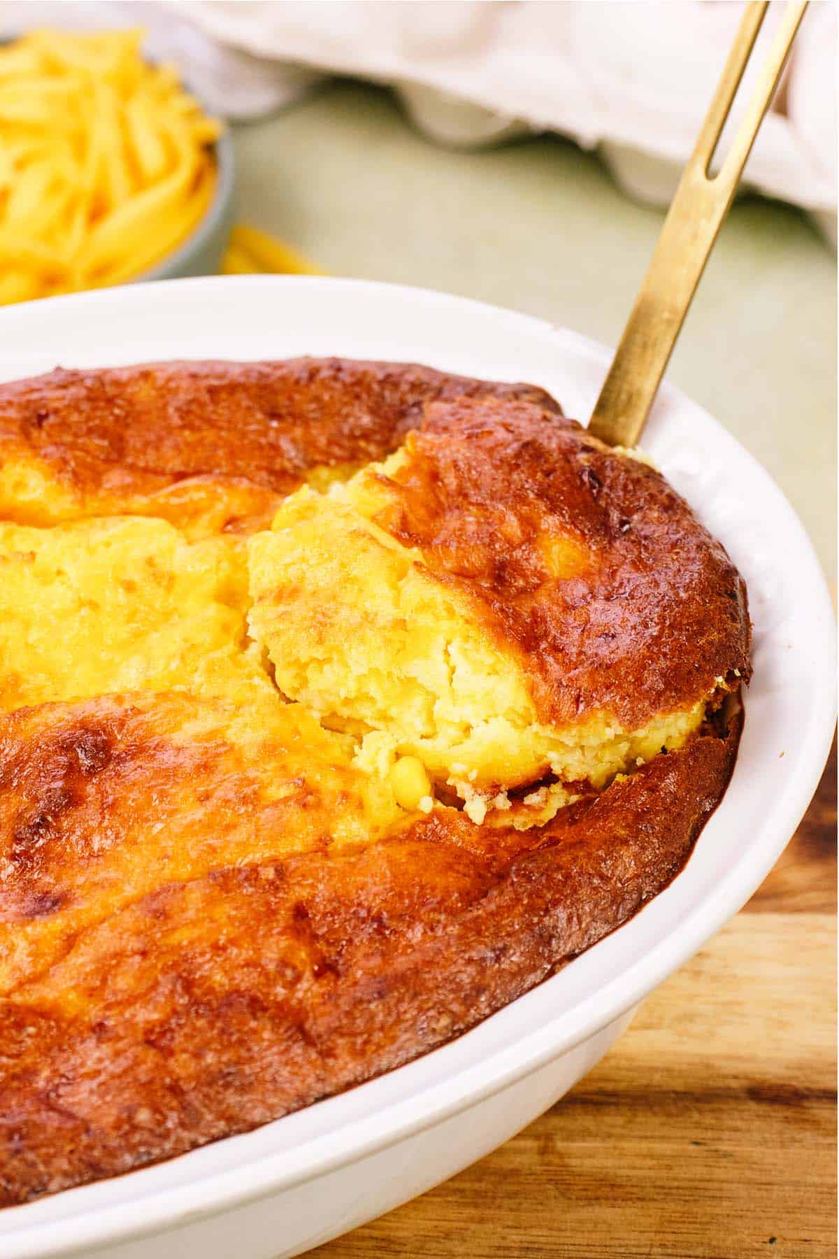 spoon lifting a serving of Corn and Cheese Pashtida Crustless Corn Quiche from a casserole dish