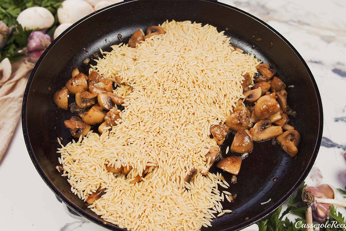 orzo being cooked with mushrooms and other ingredients in a saute pan to make Creamy Orzo Chicken Bake