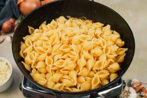 adding pasta to the skillet with the onions to make caramelized onion pasta bake