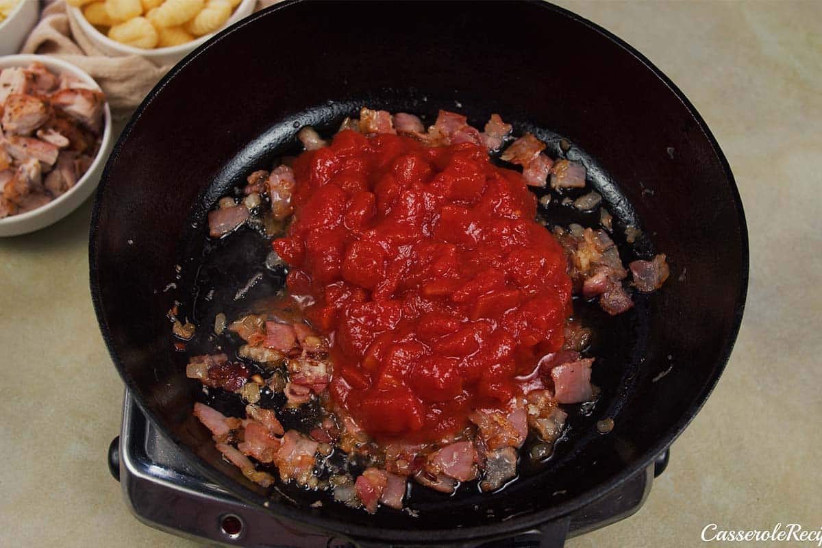 adding tomato to other ingredients to make chicken and tomato gnocchi bake