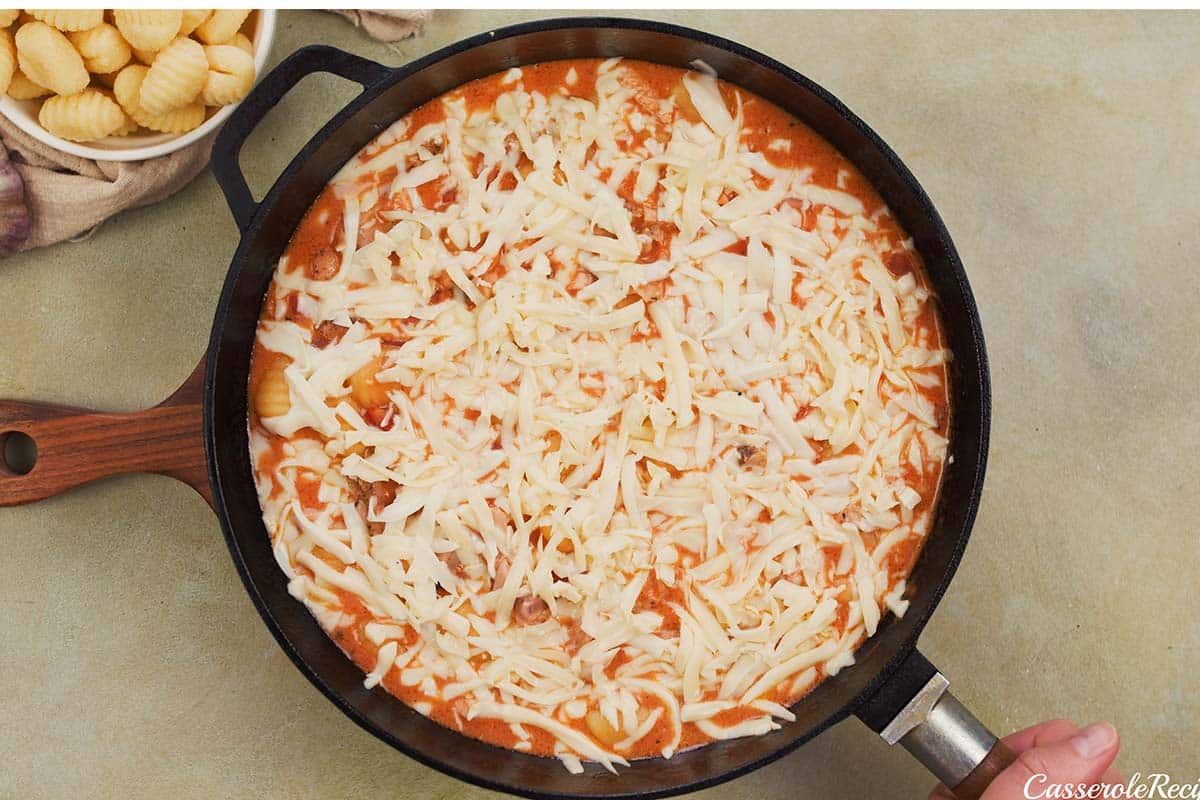 final step of covering the filling with cheese before baking chicken and tomato gnocchi bake