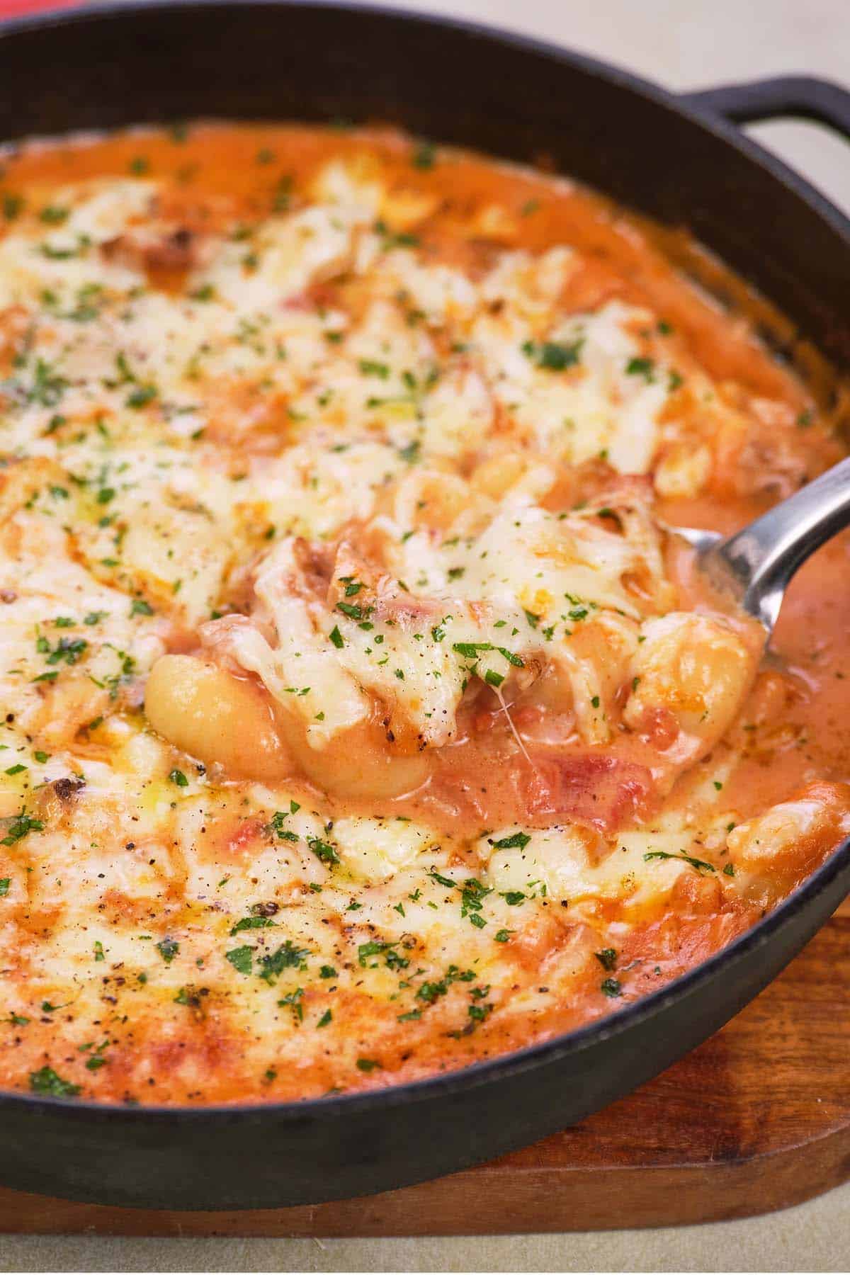 spoon serving chicken and tomato gnocchi bake from a cast iron skillet