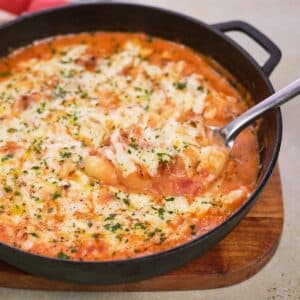 cast iron skillet with chicken and tomato gnocchi bake being served with a spoon