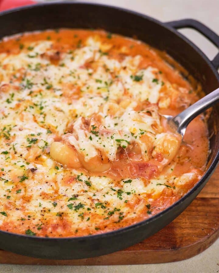 cast iron skillet with chicken and tomato gnocchi bake being served with a spoon