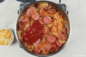 tomato sauce being added to sausage and other ingredients in a sauce pan to make Louisiana Casserole