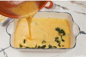 sauce being added to the filling to make spinach artichoke breakfast casserole