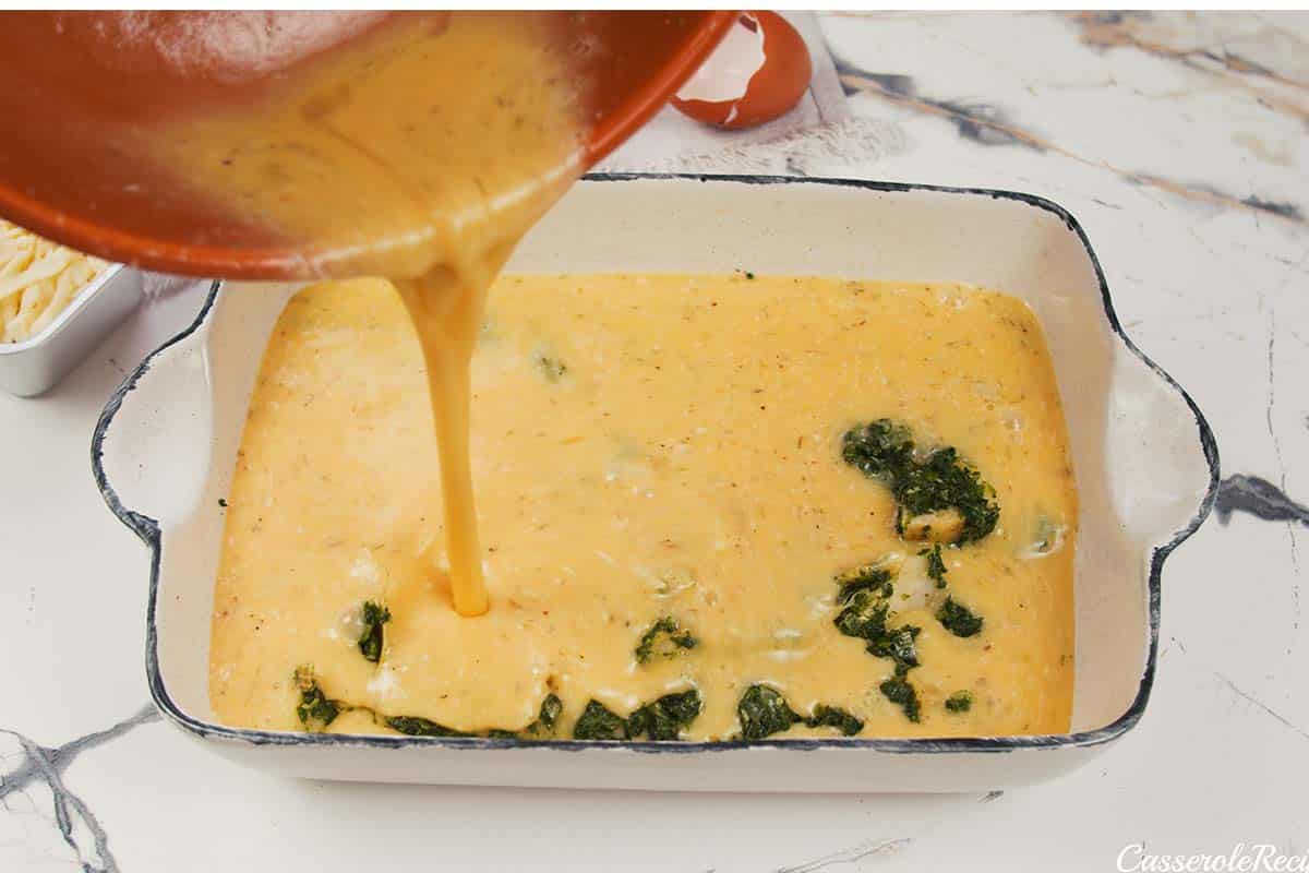 sauce being added to the filling to make spinach artichoke breakfast casserole