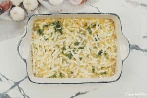 final step of adding cheese to the top of the filling to make spinach artichoke breakfast casserole prior to baking