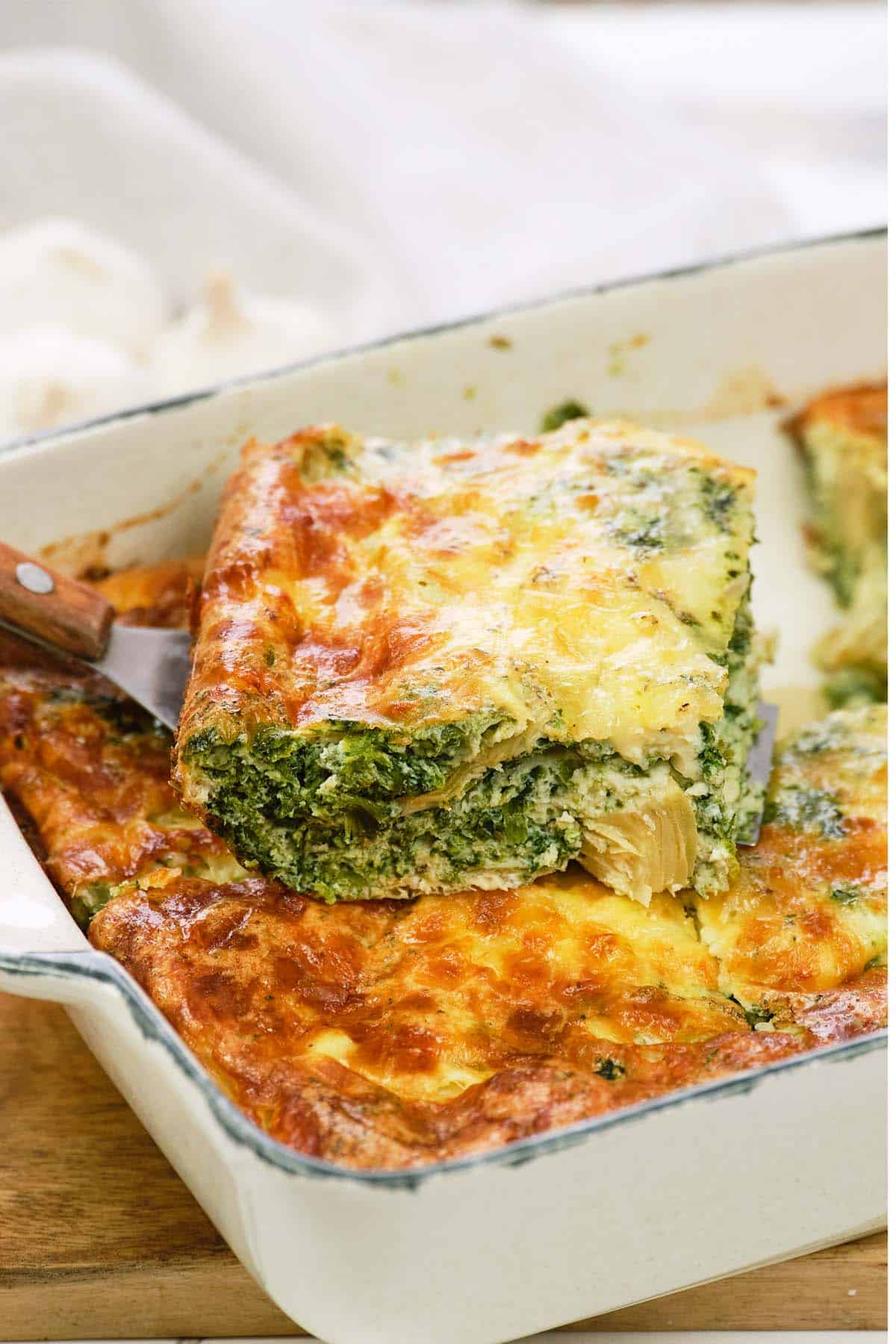 serving of spinach artichoke breakfast casserole being listed from a baking dish