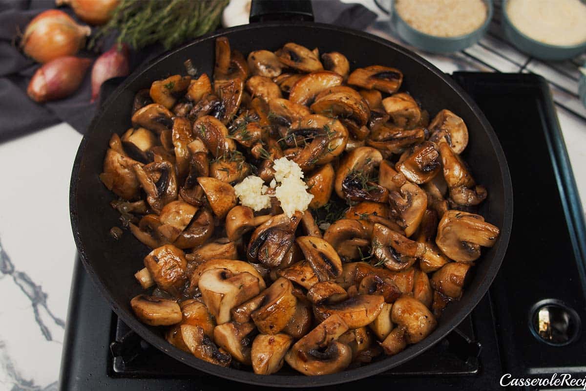 mushrooms being cooked in a saute pan with other ingredients to make stuffed mushroom casserole