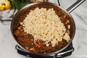 couscous being added to other ingredients in a saute pan to make Pizza Casserole with Couscous