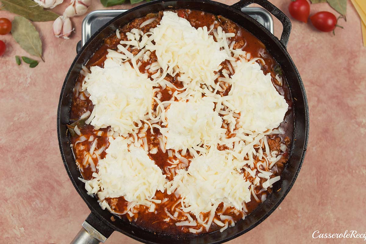 last step of making cheat lasagne bake by topping with cheese prior to baking