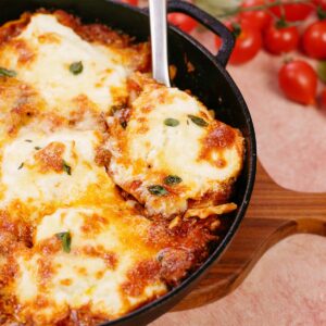 spoon lifting a serving of cheat lasagne bake from a cast iron skillet
