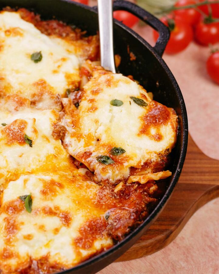 spoon lifting a serving of cheat lasagne bake from a cast iron skillet