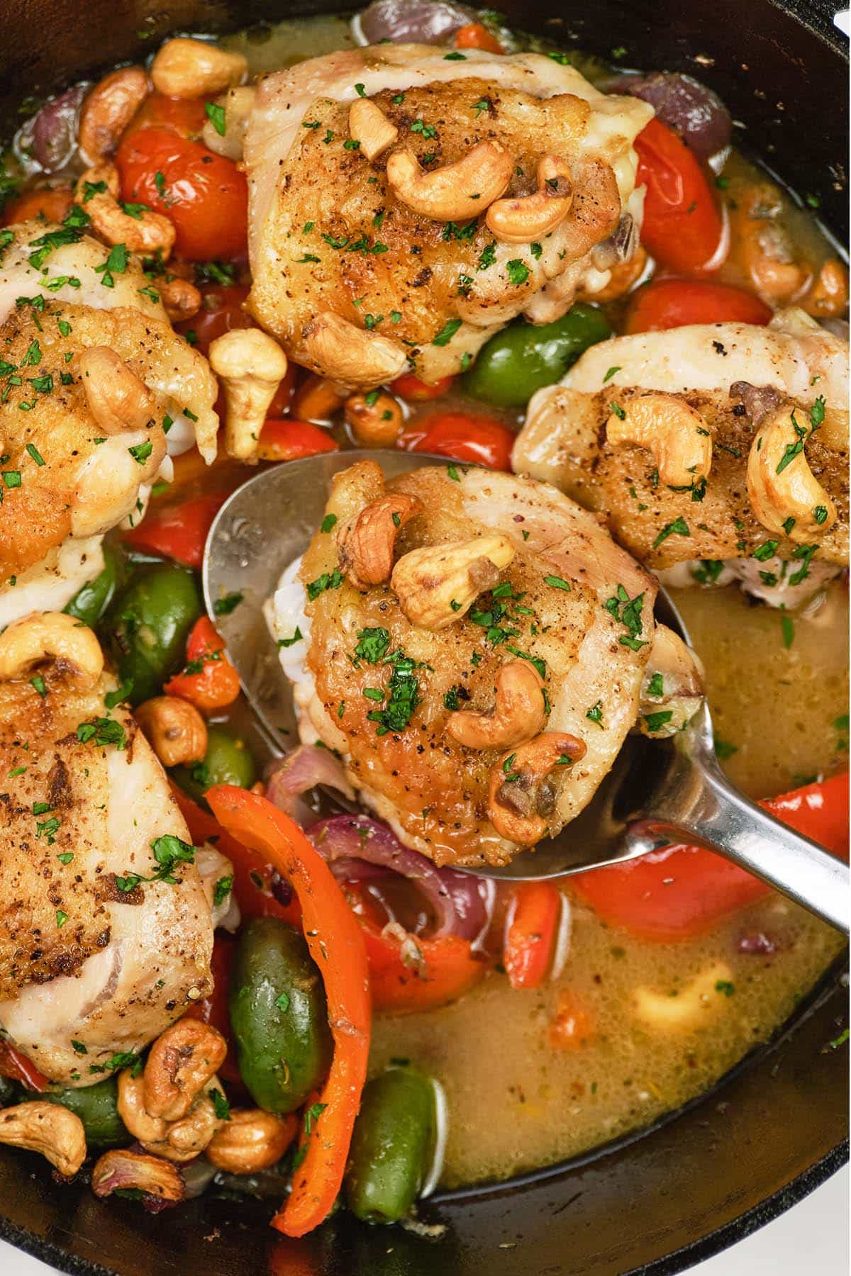 spoon lifting a serving of chicken bake with anchovy cashew from a skillet
