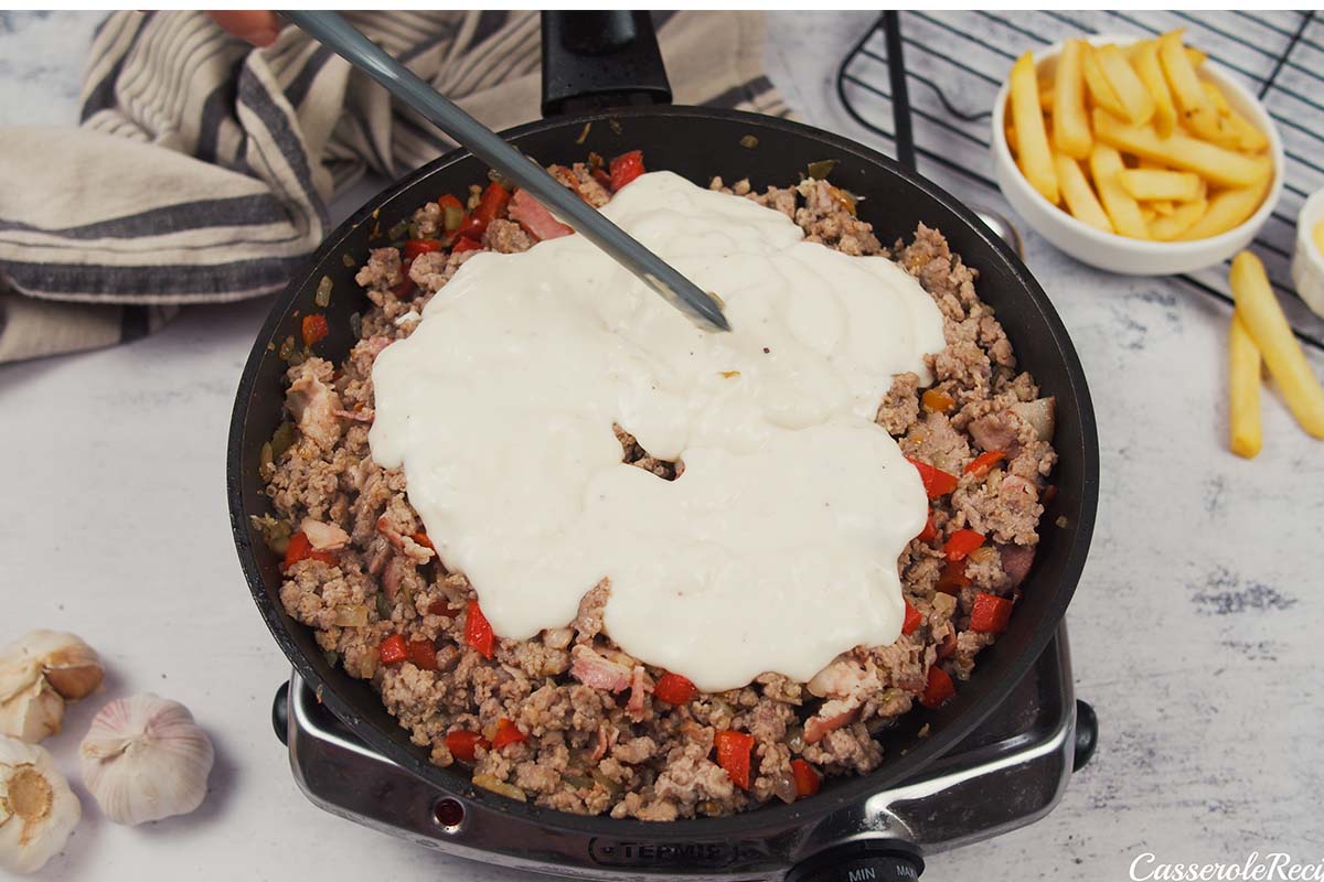 bechamel sauce being added to filling ingredients to make french fry casserole