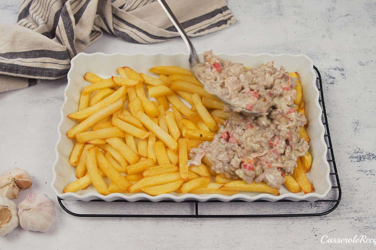 filling being spooned over french fries in a baking dish to make french fry casserole