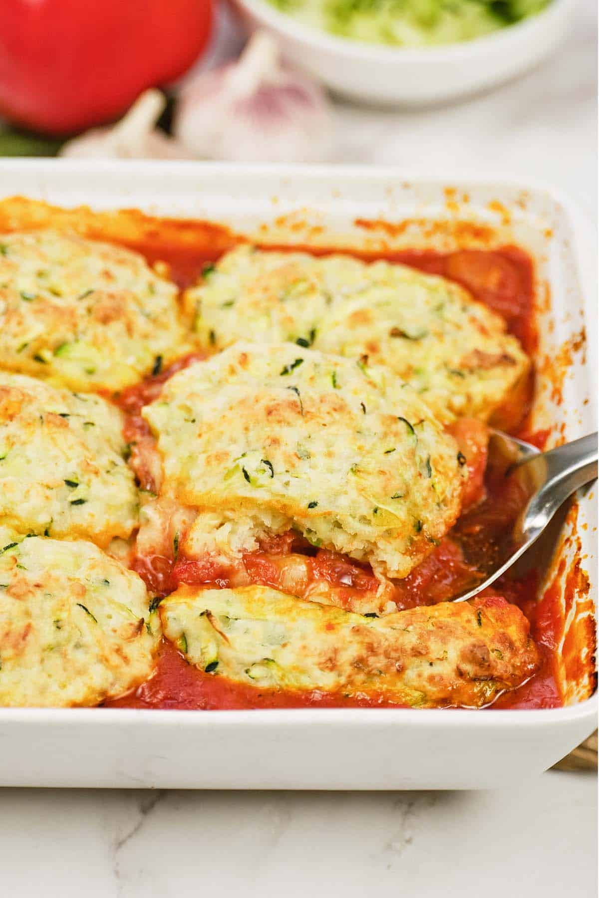 baking dish of greek casserole with zucchini dumplings being served with a large spoon