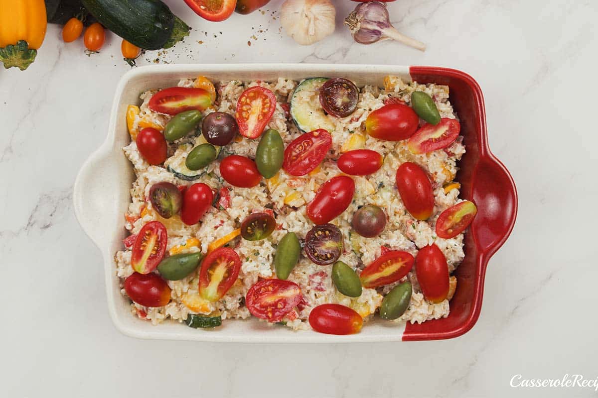 final step of making greek vegetable casserole by topping with tomatoes and basil