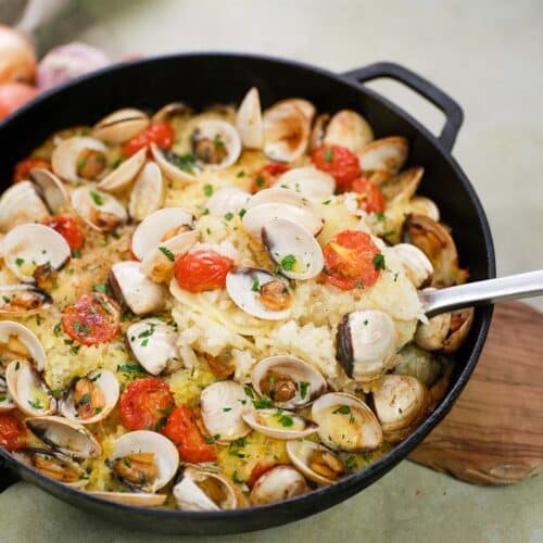 cast iron skillet of italian baked rice and clams being served with a big spoon