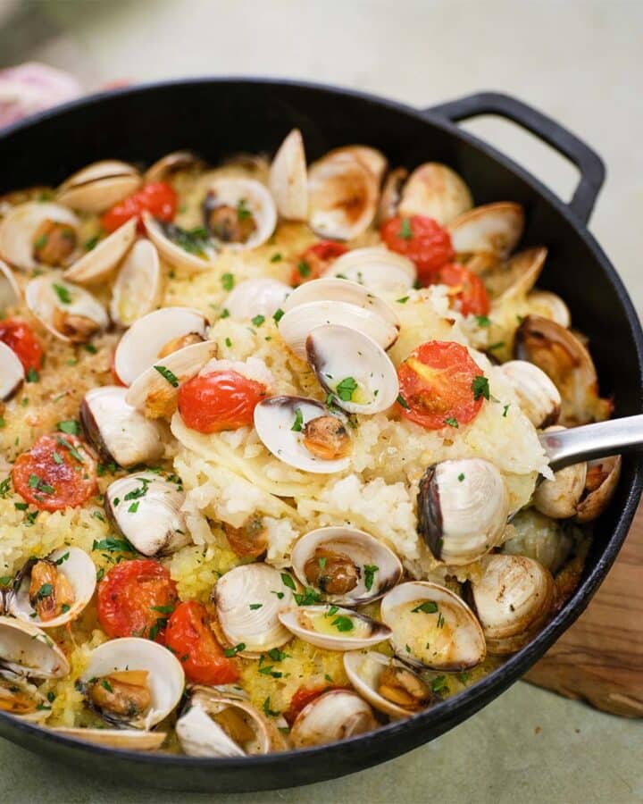 cast iron skillet of italian baked rice and clams being served with a big spoon