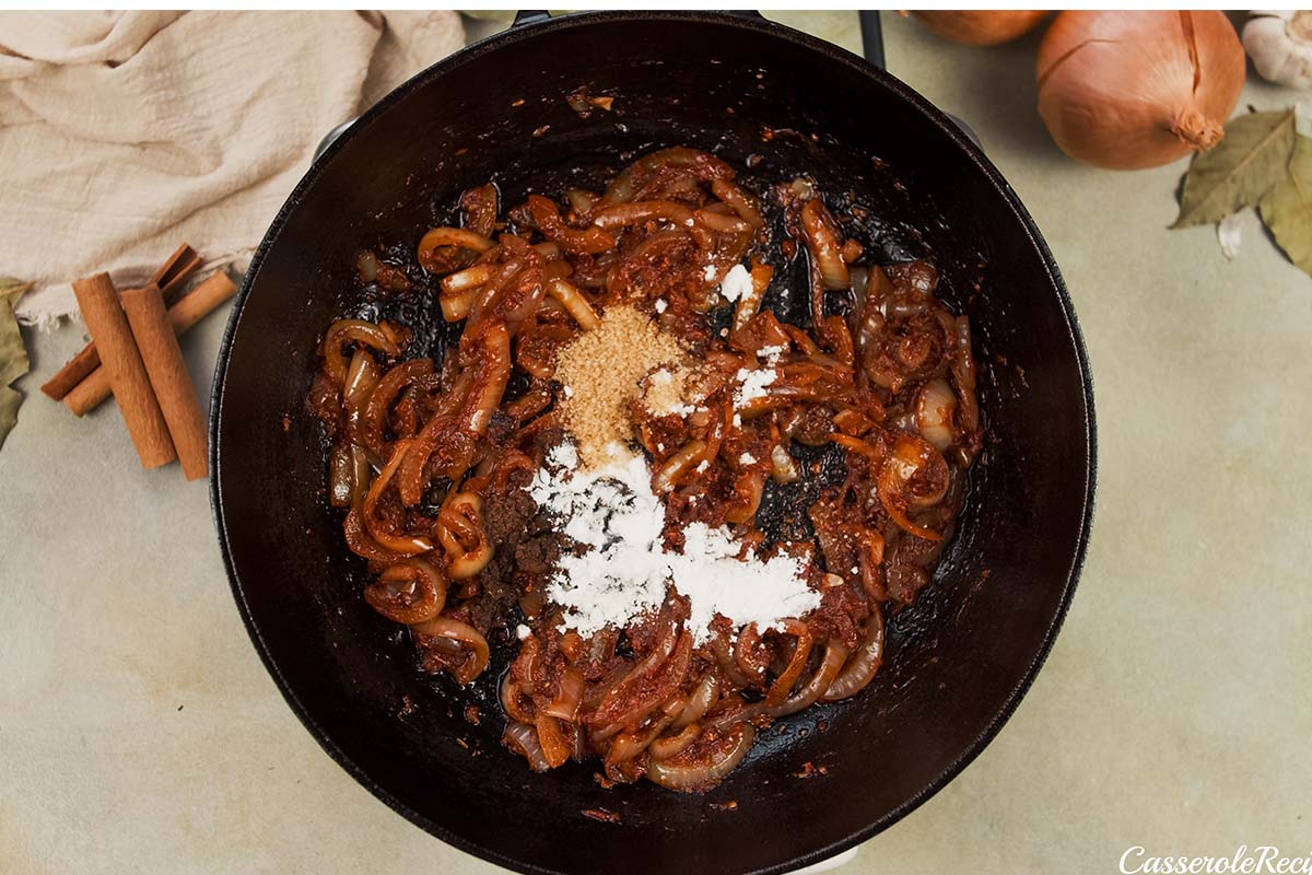 flour being added with other seasonings to caramelized onions to make kebab casserole