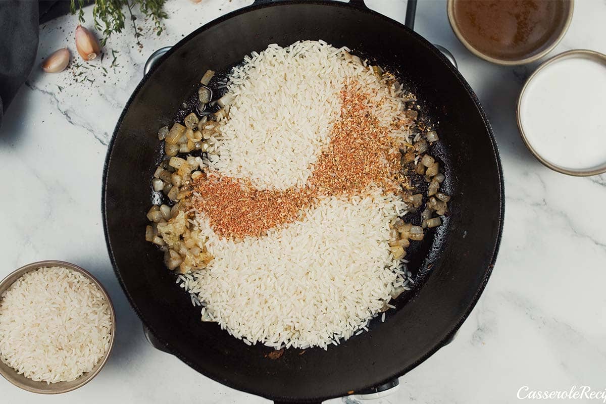 rice and seasoning being added to a cast iron skillet to make One Pot Caribbean Jerk Chicken & Rice