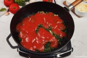 tomato sauce being added to spinach and other ingredients to make Baked Orecchiette with Spinach
